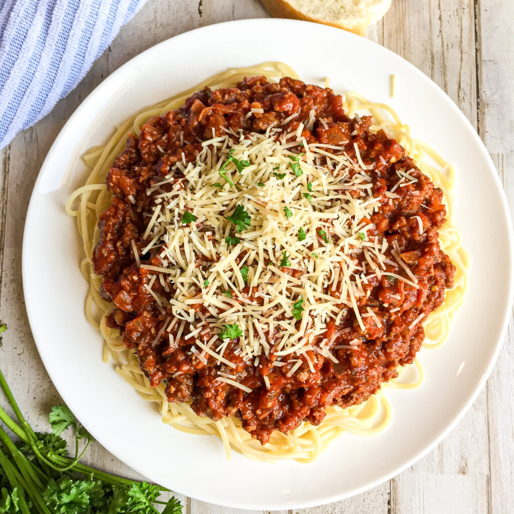 spaghetti sauce with  noodles on a round white plate with shredded parmesan cheese and fresh basil