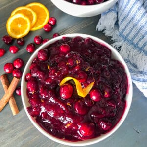 homemade cranberry sauce in a serving dish with orange slices, fresh cranberries, and cinnamon sticks for garnish
