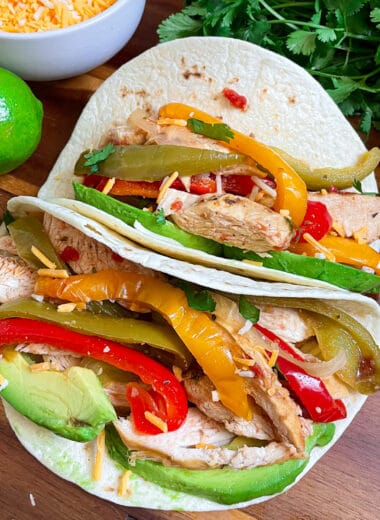 slow cooker chicken fajitas served in tortillas with lime, cheese, and cilantro