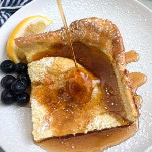 German pancakes on a serving plate with blueberries, lemon and maple syrup