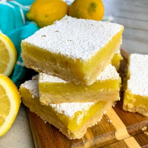 Lemon bars stacked up on a wood cutting board.