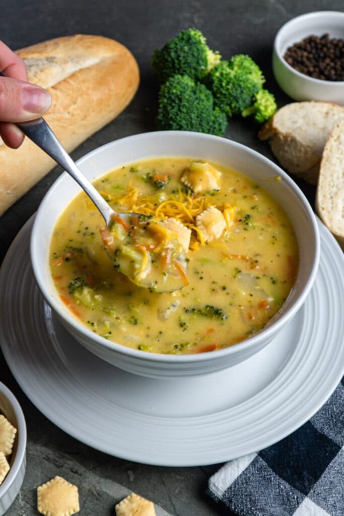 A spoonful of broccoli cheese soup lifted from a bowl filled with soup.