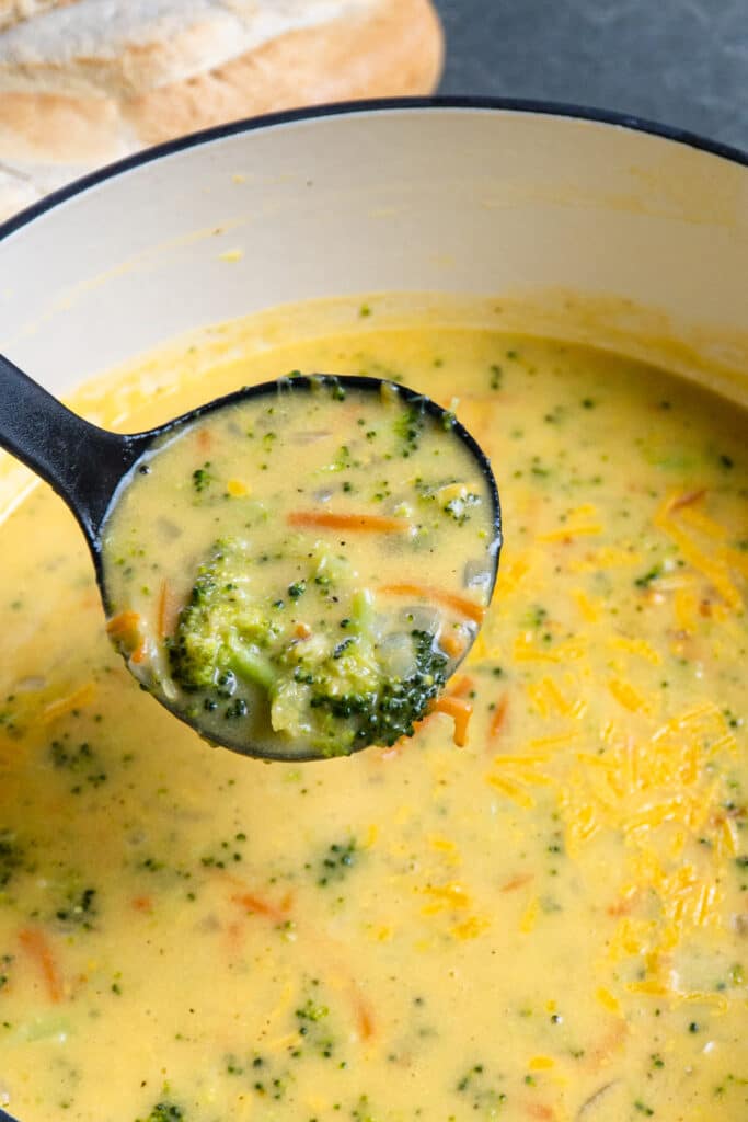 Broccoli cheese soup in a pot with a scoop in a laddle.