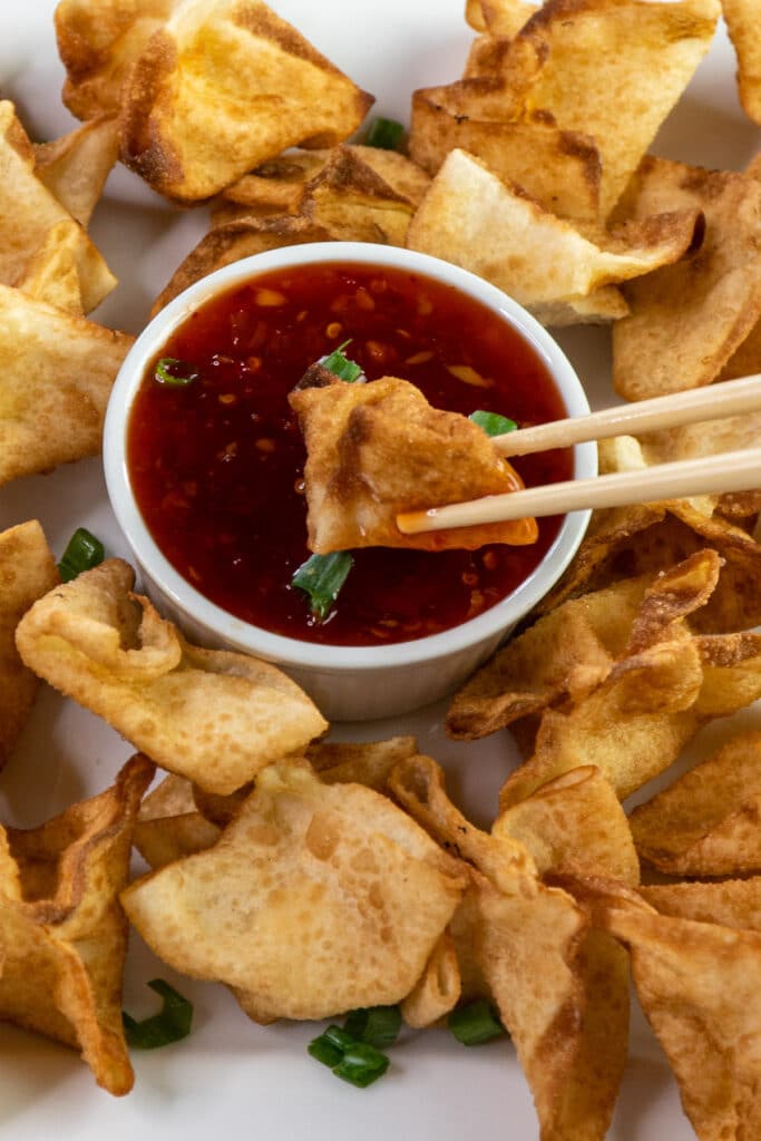 Cream cheese wonton being dipped into sweet chili sauce.