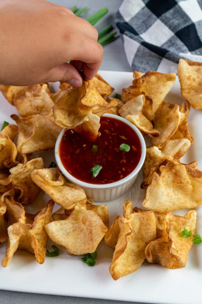 Crab Rangoon being dipped into sweet chili sauce.