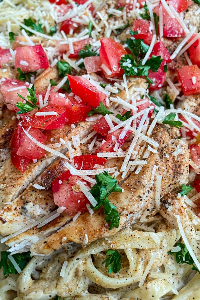 the most amazing Cajun chicken alfredo with diced tomatoes, chopped parsley, and shredded parmesan cheese