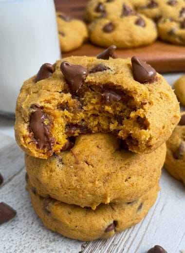 The best soft and chewy pumpkin chocolate chip cookies stacked on top of each other served with a glass of milk