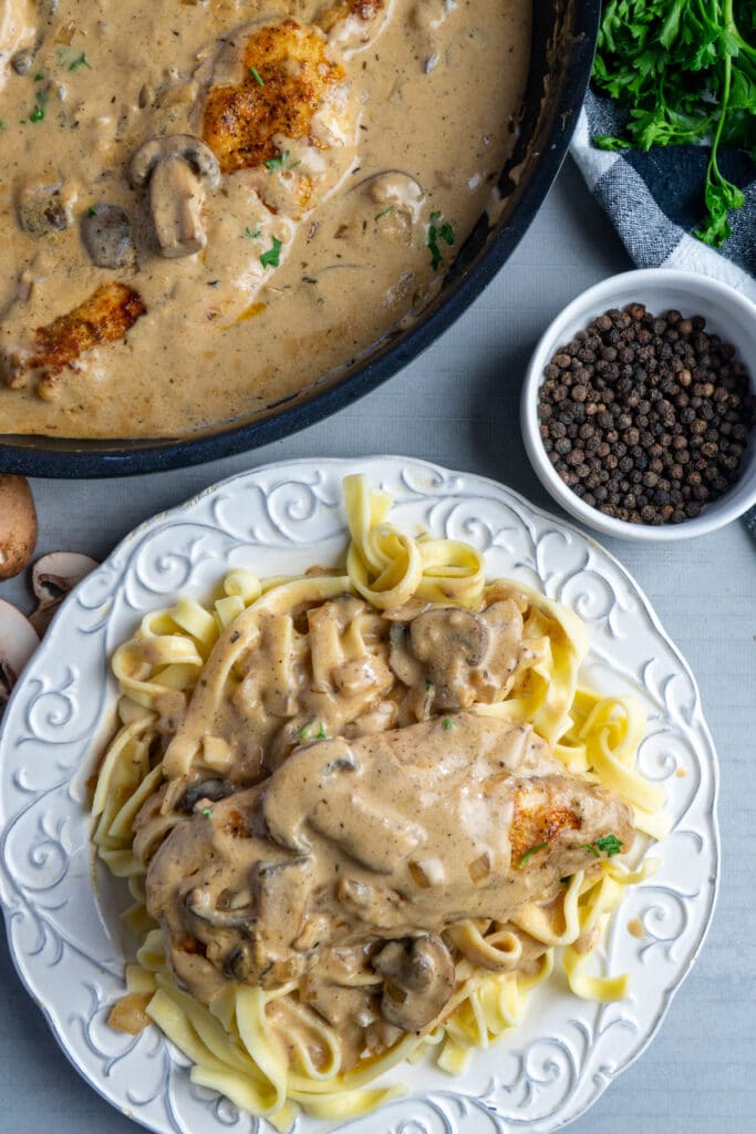 Creamy chicken stroganoff on a white plate over the top of noodles.