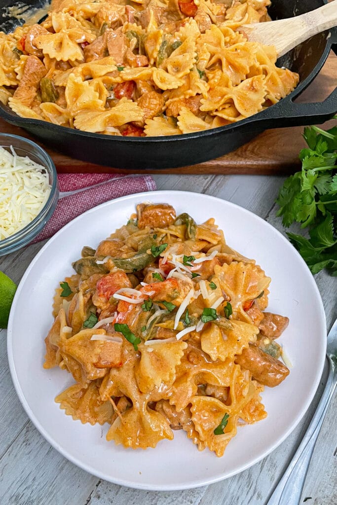 Creamy chicken fajita pasta served on a white serving plate topped with shredded cheese and chopped cilantro.