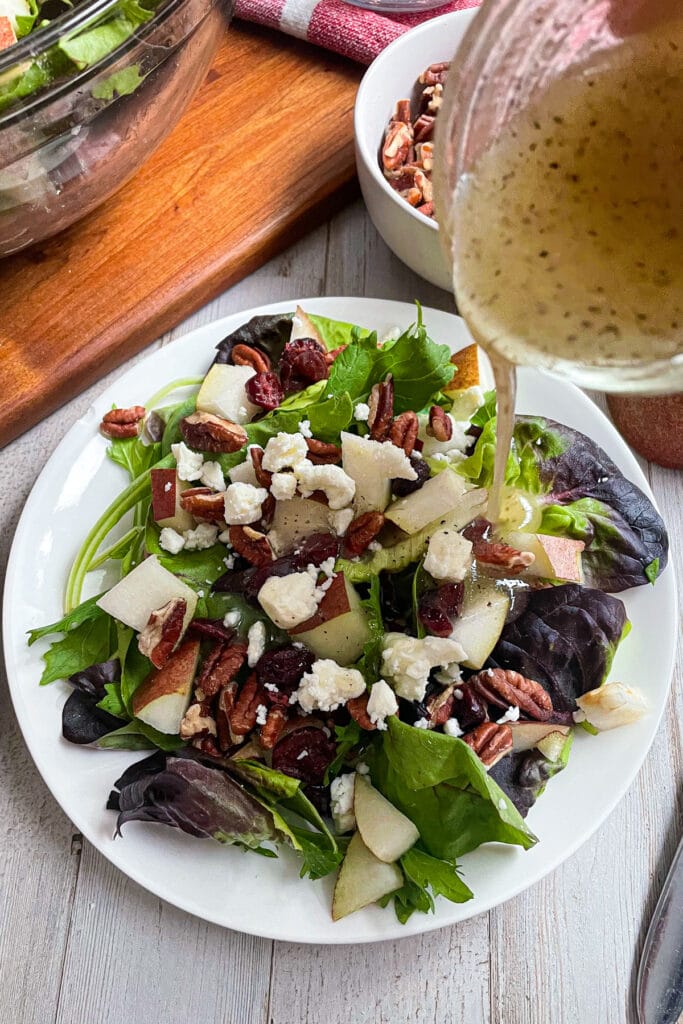 Autumn pear salad with homemade honey mustard dressing being poured on salad