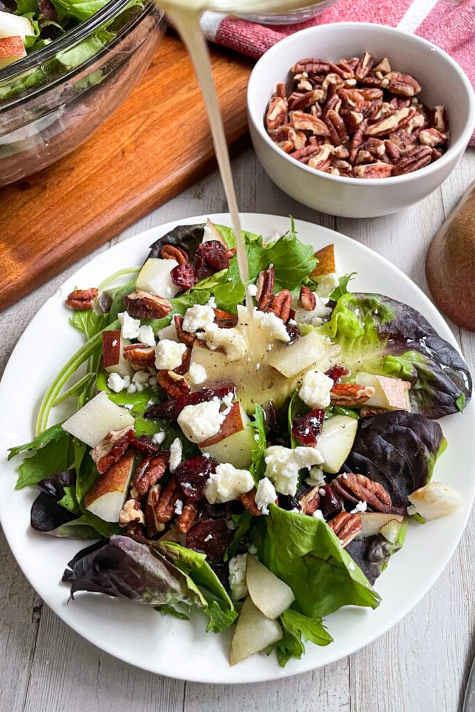 Autumn pear salad with honey mustard dressing being poured on top of salad