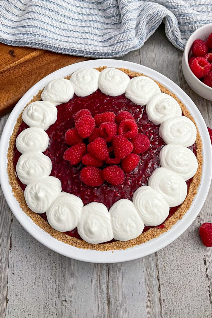 assembled raspberry cream pie with a side dish of fresh raspberries