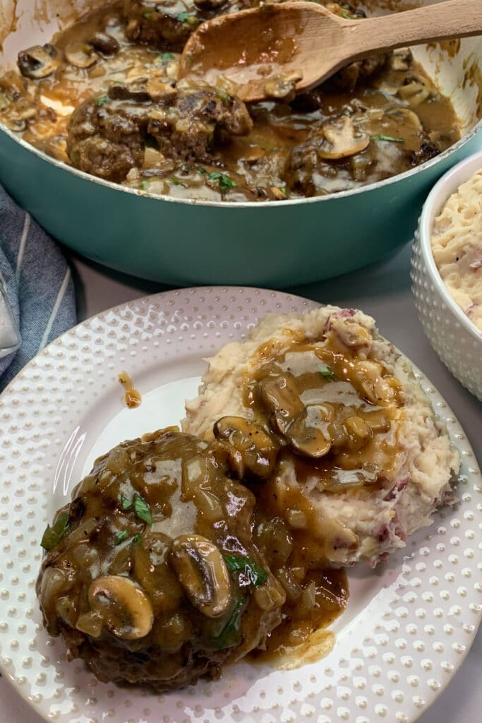 Salisbury steak on a white plate with garlic mashed potatoes.
