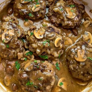 Salisbury steak in a skillet and garnished with fresh chopped parsley.