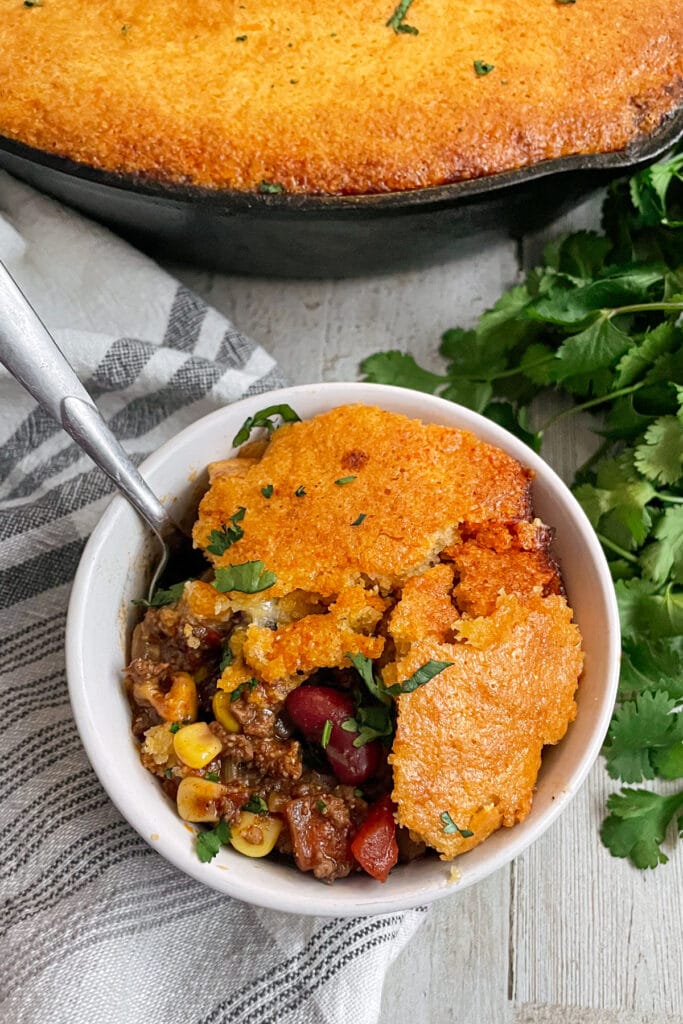 Cornbread chili pie served in a white bowl with chopped cilantro