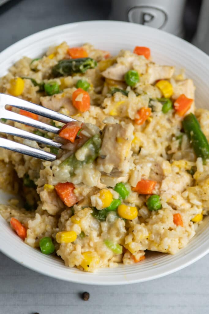 Slow cooker chicken and rice in a white bowl with a bite of it on fork.