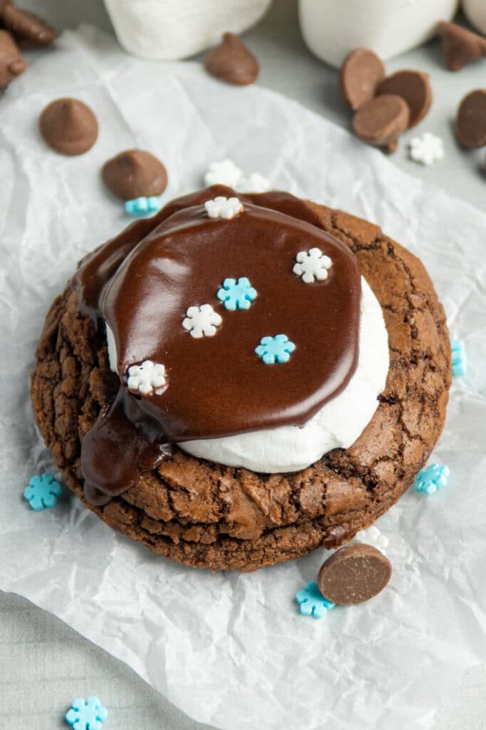 One hot chocolate cookie with jumbo marshmallows on a piece of parchment paper.
