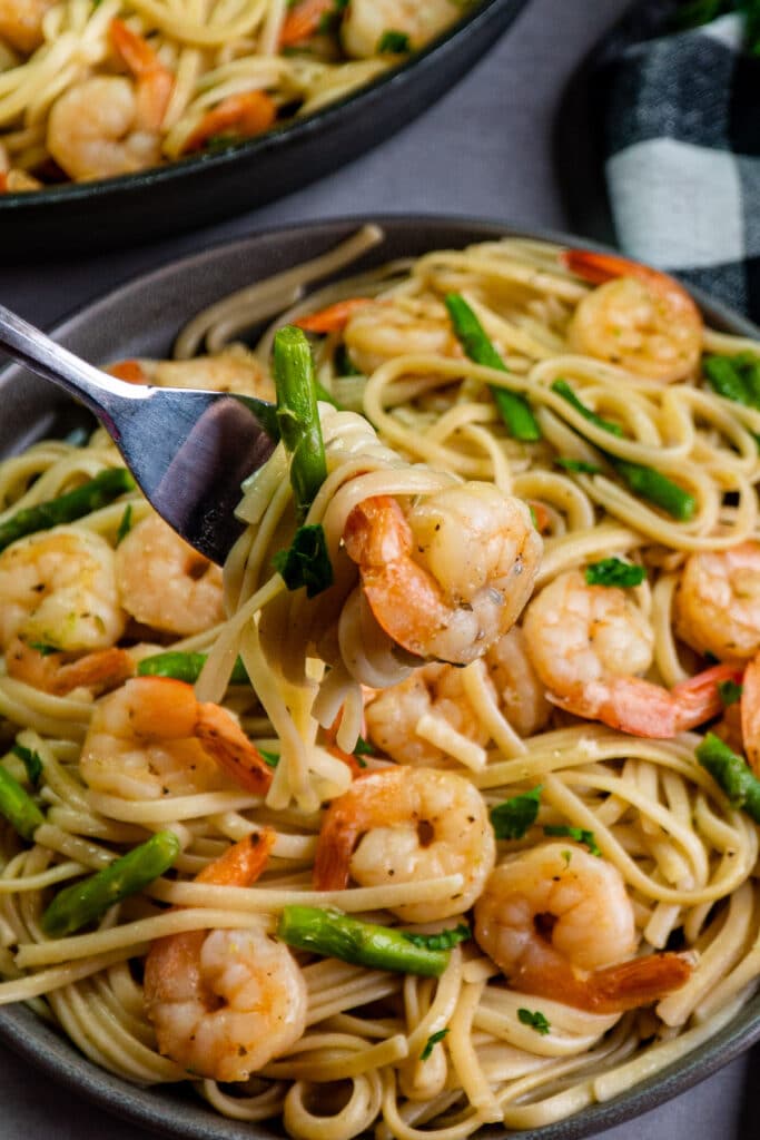 Close up of shrimp scampi on a plate being picked up on a fork.