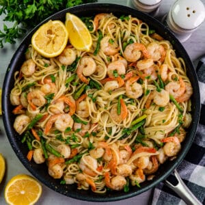 Shrimp scampi with pasta and asparagus in a skillet with fresh lemons.