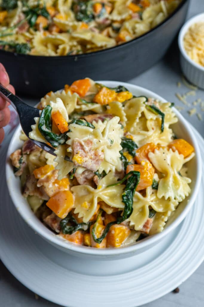 Creamy butternut squash pasta with bacon in a white bowl with a bite on a fork.