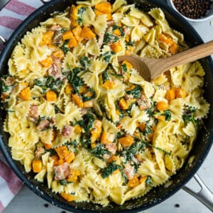 Creamy butternut squash pasta with bacon in a skillet with a large wooden spoon in it.