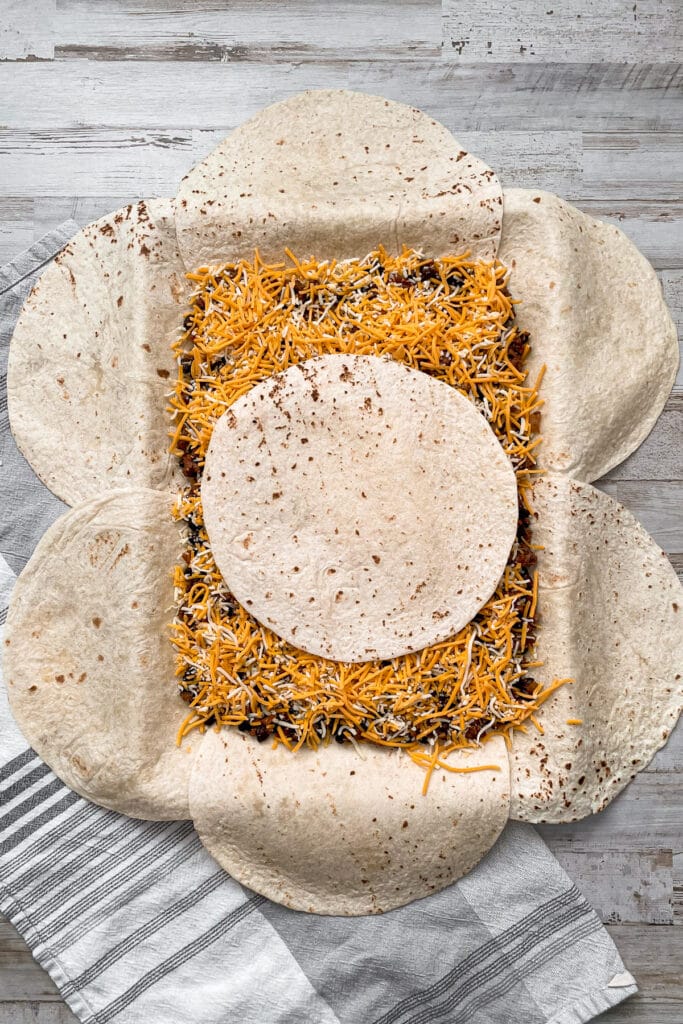 sheet pan quesadillas lined with tortillas, meat mixture, cheese