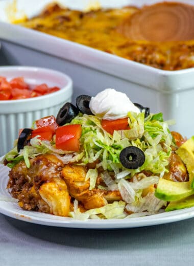 Mexican bubble pizza on a white plate topped with tomatoes, lettuce, olives, and sour cream.