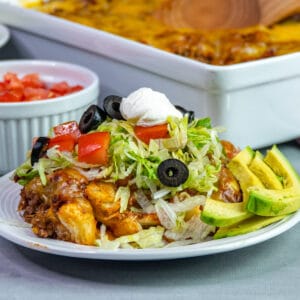 Mexican bubble pizza on a white plate topped with tomatoes, lettuce, olives, and sour cream.