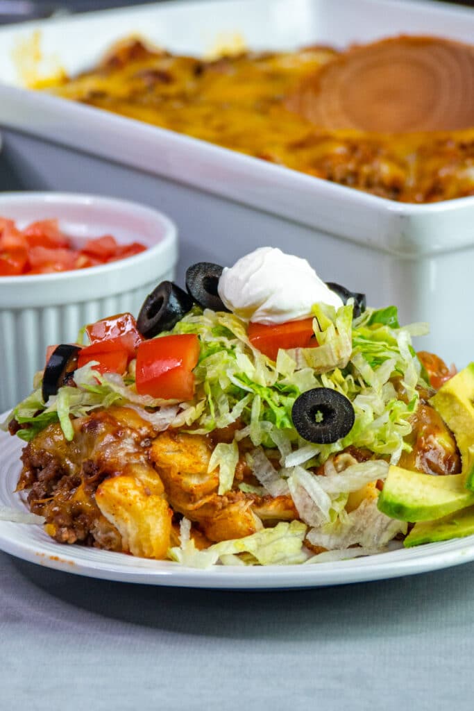 Mexican bubble pizza on a white plate topped with tomatoes, lettuce, olives, and sour cream.