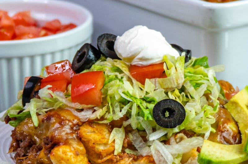 Mexican bubble pizza on a white plate topped with tomatoes, lettuce, olives, and sour cream.