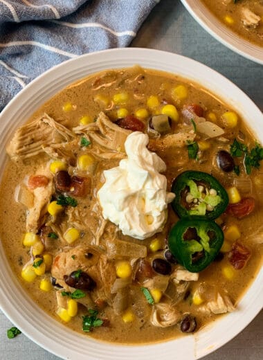 Slow cooker chicken enchilada soup in a white bowl garnished with sour cream and jalapenos.
