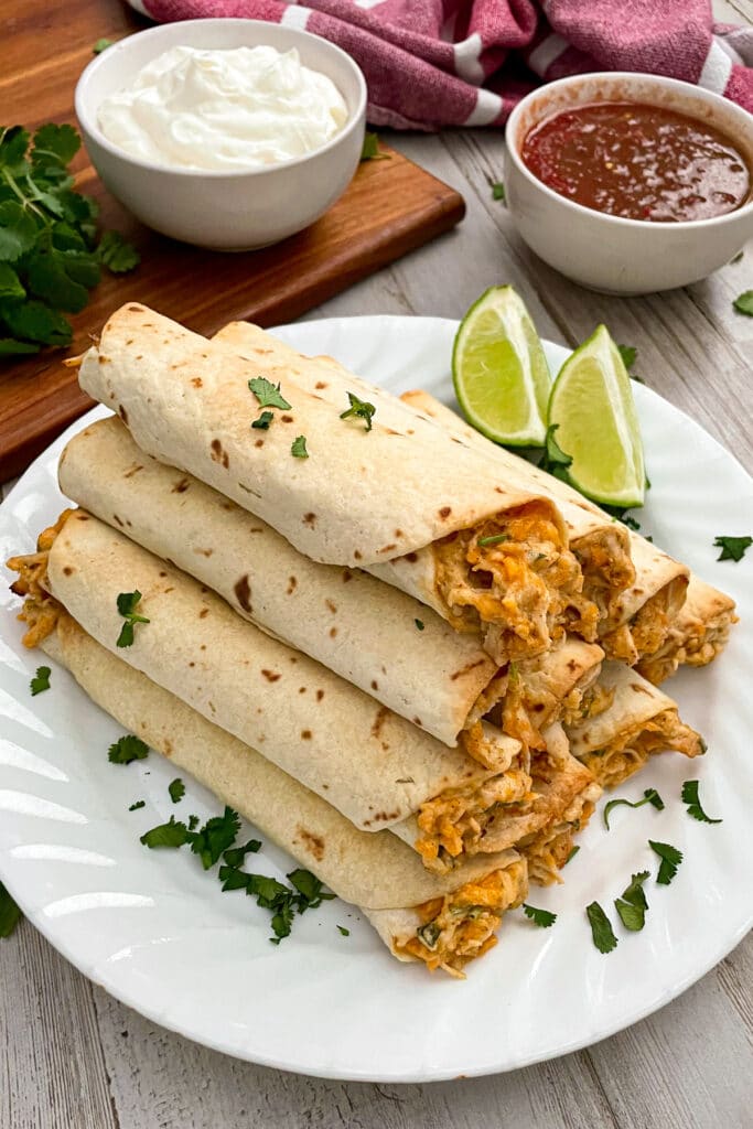 rolled chicken taquitos stacked on top of each other served on a plate