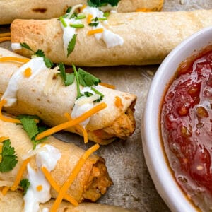 close up shot of crispy oven baked taquitos with shredded cheese and salsa