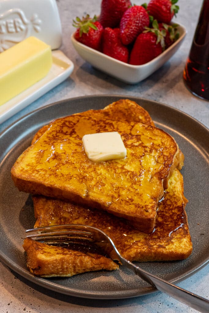 Close up of brioche Frech toast on a dark plate with butter and maple syrup on top.