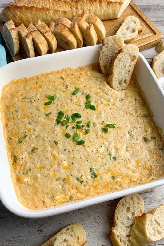 Hot cheesy crab dip in a white baking dish with slices of bread around it.