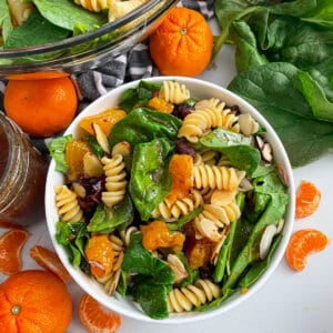 mandarin spinach pasta salad in a serving bowl with oranges and spinach on the side