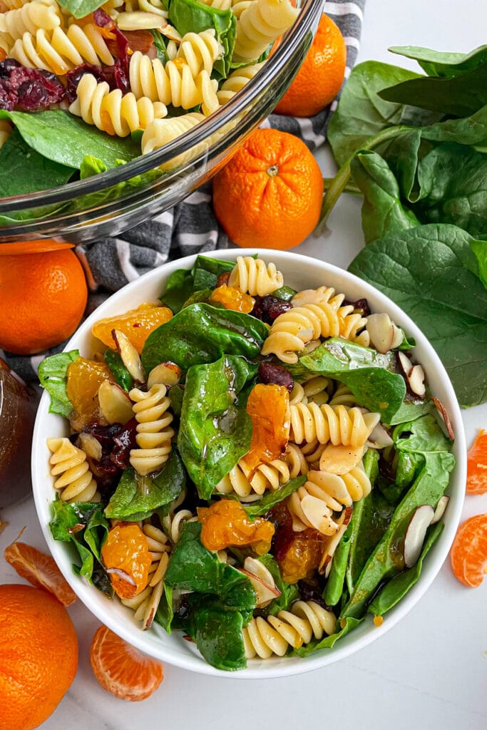 mandarin spinach pasta salad in a serving bowl with oranges on the side