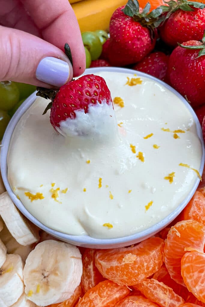 close up shot of lemon cream fruit dip with a strawberry dipped in it