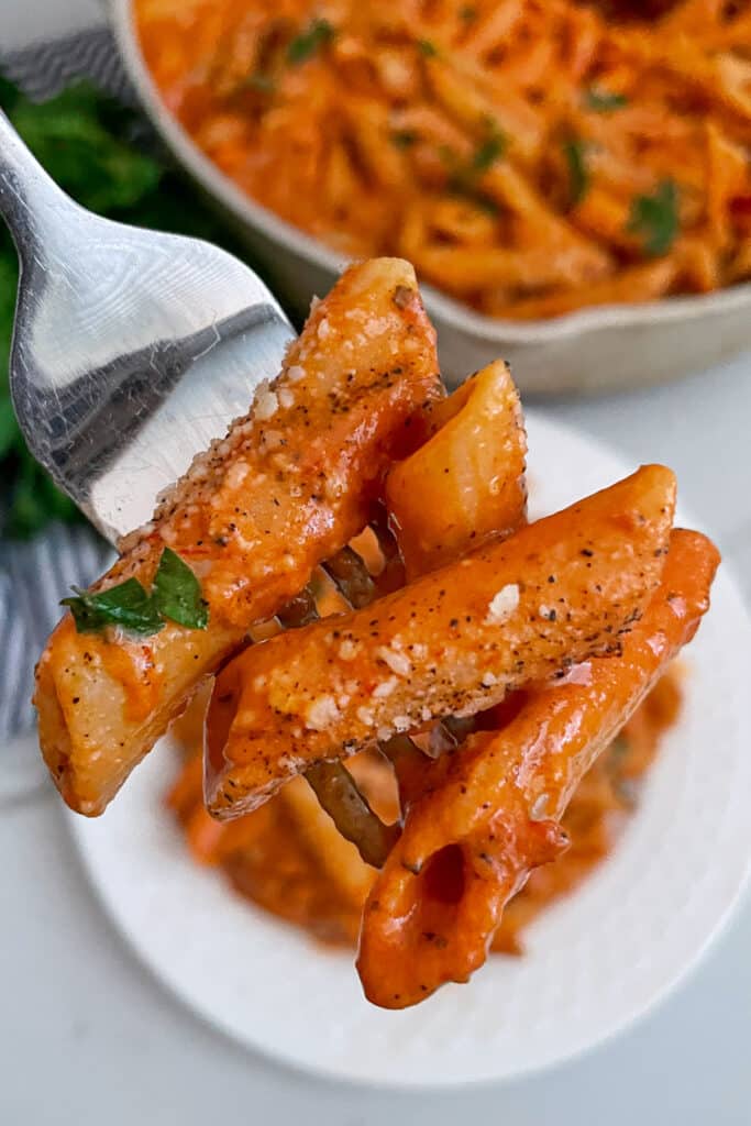 Close up photo of penne rosa on a fork with parmesan cheese and shredded parsley