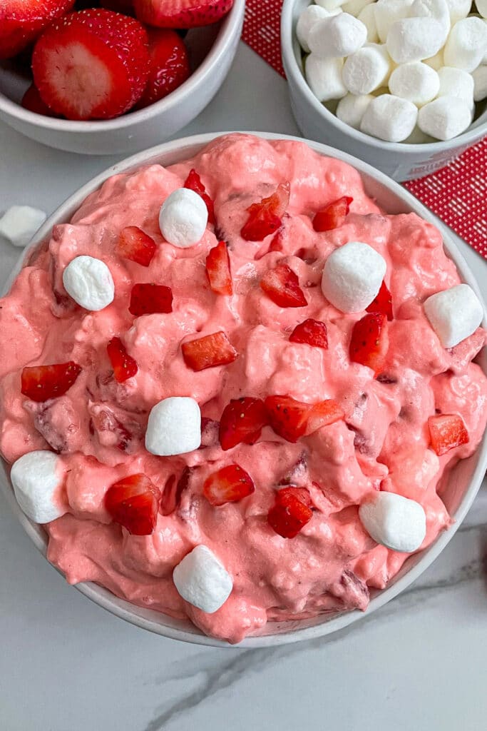 strawberry fluff jello salad in a serving bowl with marshmallows and strawberries on the side