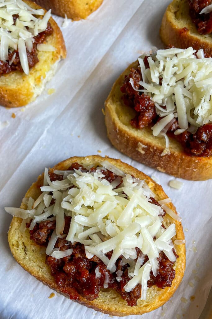 Unbaked Texas toast sloppy joes with shredded cheese on top placed on a baking pan with parchment paper