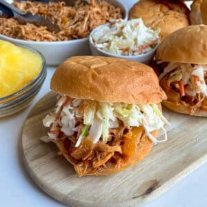 close up photo of slow cooker Hawaiian chicken with pineapple slaw on a hamburger bun with pineapple on the side