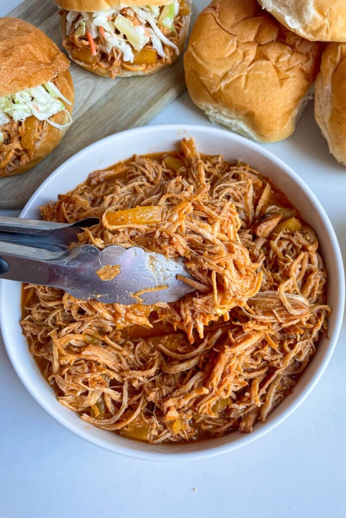 slow cooker Hawaiian chicken with pineapple slaw in a white serving bowl with buns for serving