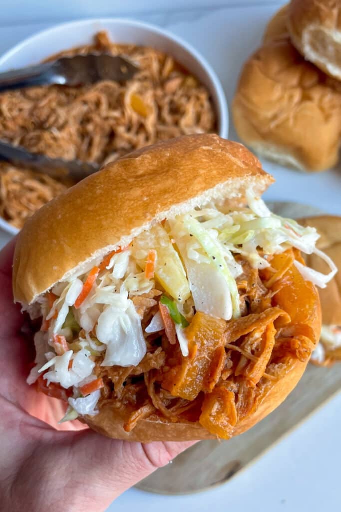 slow cooker Hawaiian chicken with pineapple slaw on a hamburger bun with pork in a serving bowl