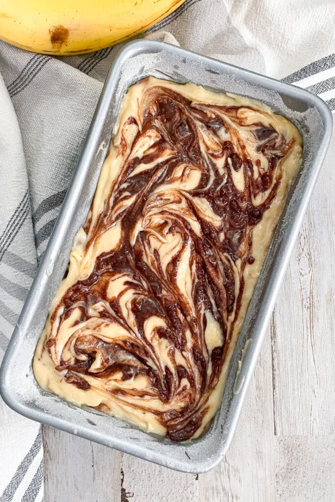 cinnamon swirl banana bread batter in a baking pan with a banana on the side