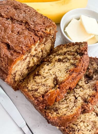 cinnamon swirl banana bread cut into slices with butter and bananas on the side