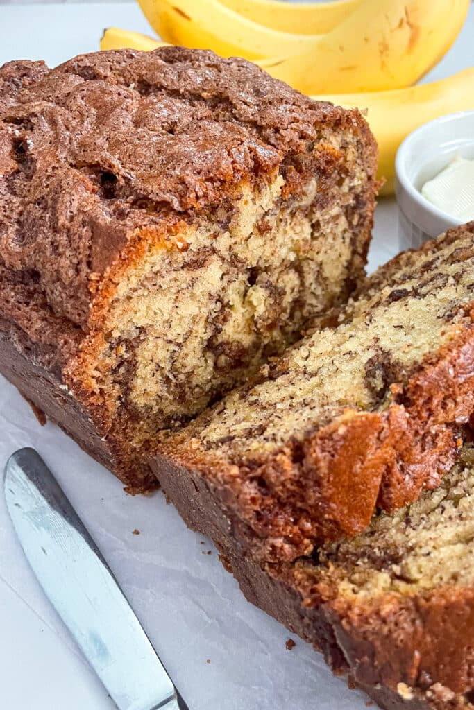 cinnamon swirl banana bread cut into slices with a knife and bananas in the background