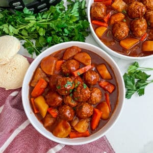 Meatball pot roast in two white serving bowls with sliced bread on the side