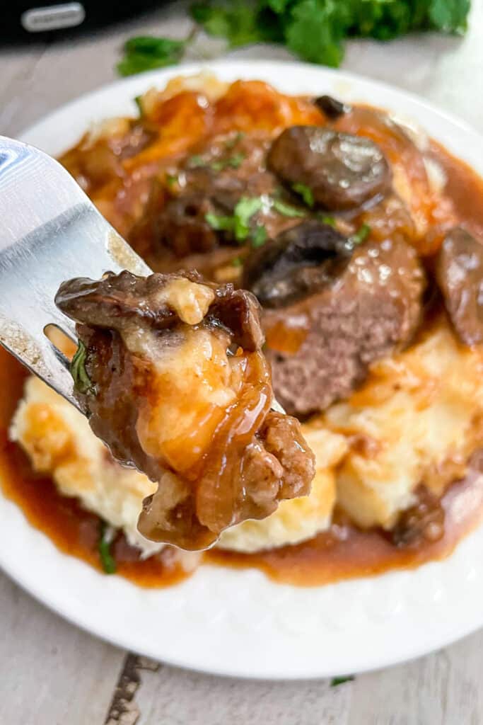 Close up photo of mashed potatoes, salisbury steak, and mushrooms on a fork