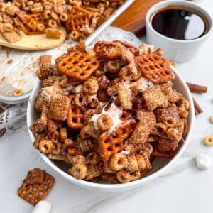Pumpkin Spice Chex Mix in a white serving bowl with a bowl of maple syrup and cinnamon sticks